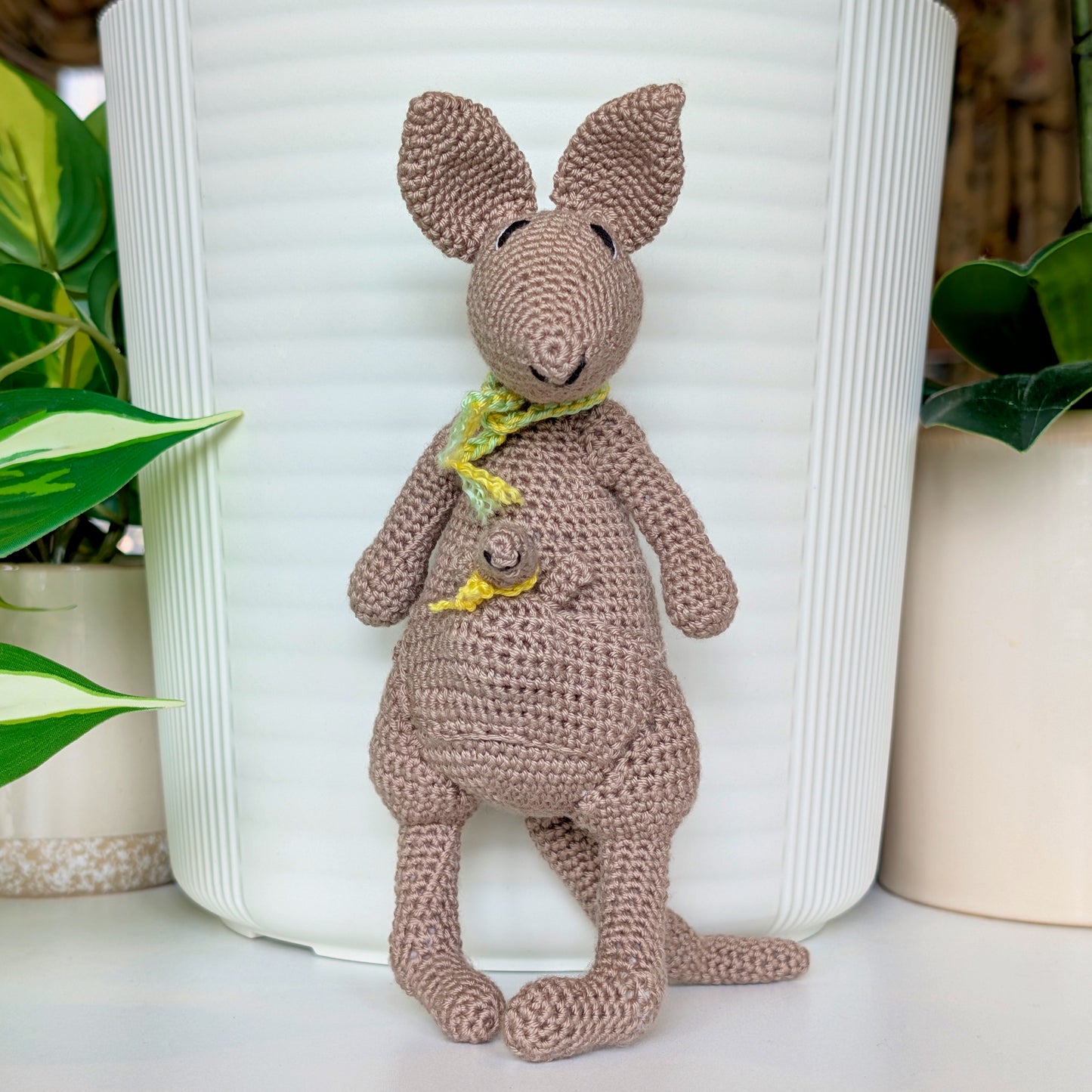 Crocheted kangaroo wearing a mint green and yellow scarf with a baby joey in her pouch also wearing a yellow scarf