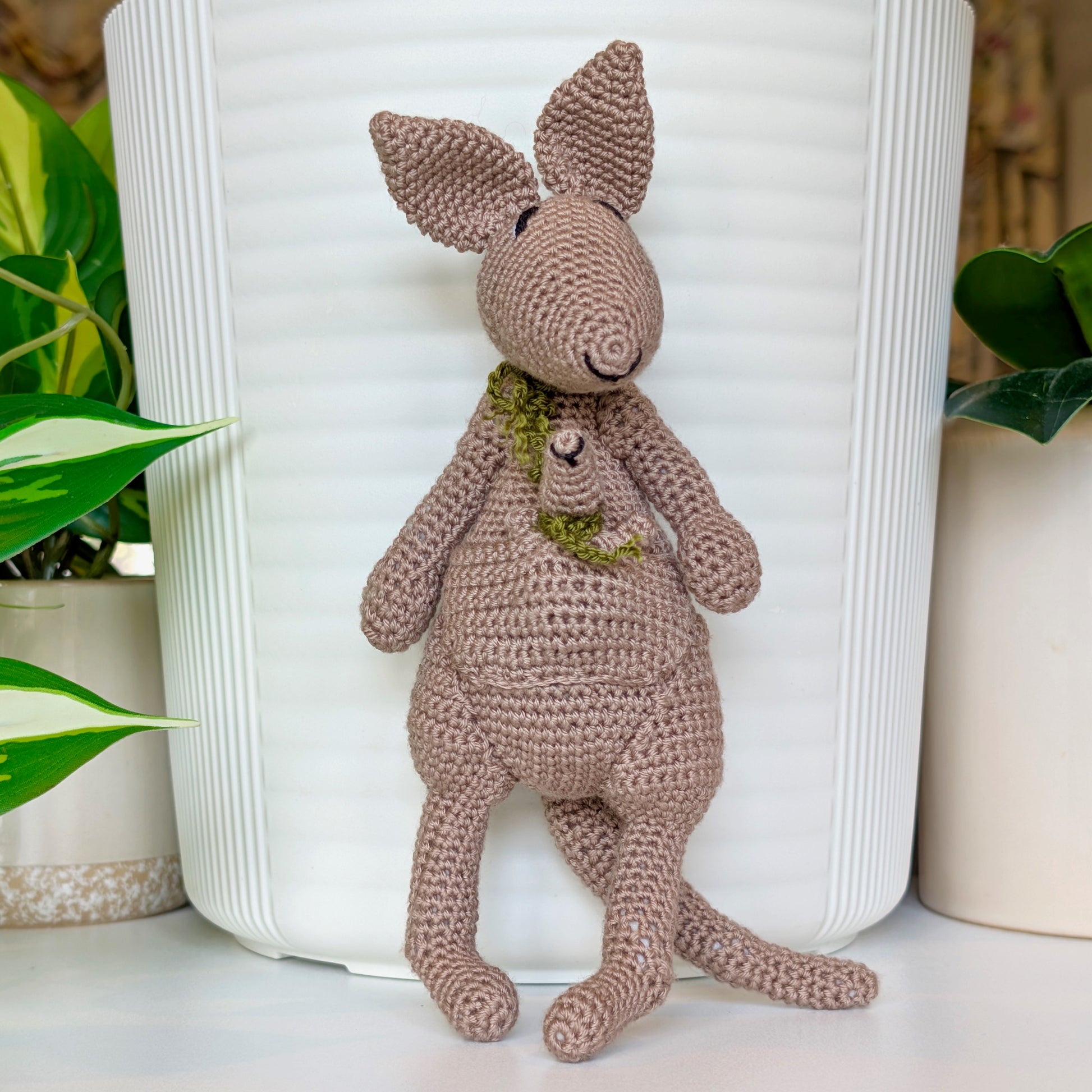 Crocheted kangaroo wearing an olive scarf with a baby joey in her pouch also wearing an olive scarf
