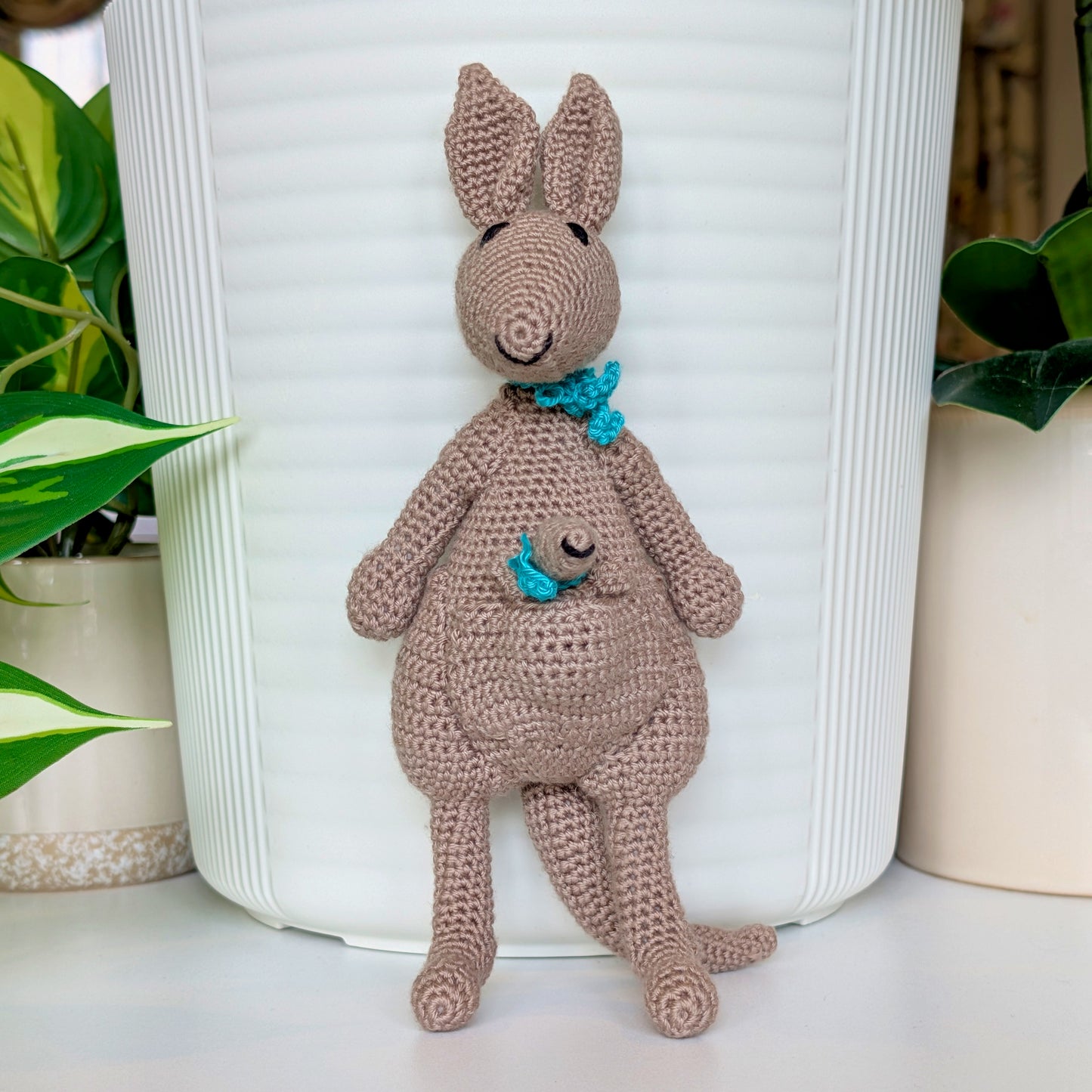 Crocheted kangaroo wearing a teal scarf with a baby joey in her pouch also wearing a teal scarf