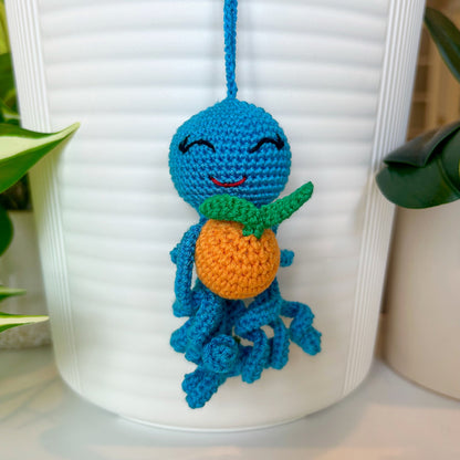 crocheted azure octopus charm with squinting eyes holding a tangerine