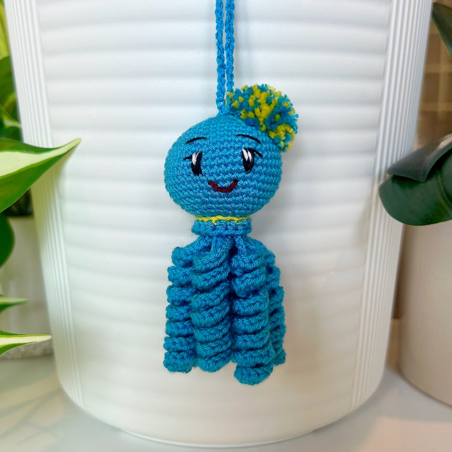 Crocheted azure octopus charm with a yellow and blue pom pom and scarf and curly tentacles