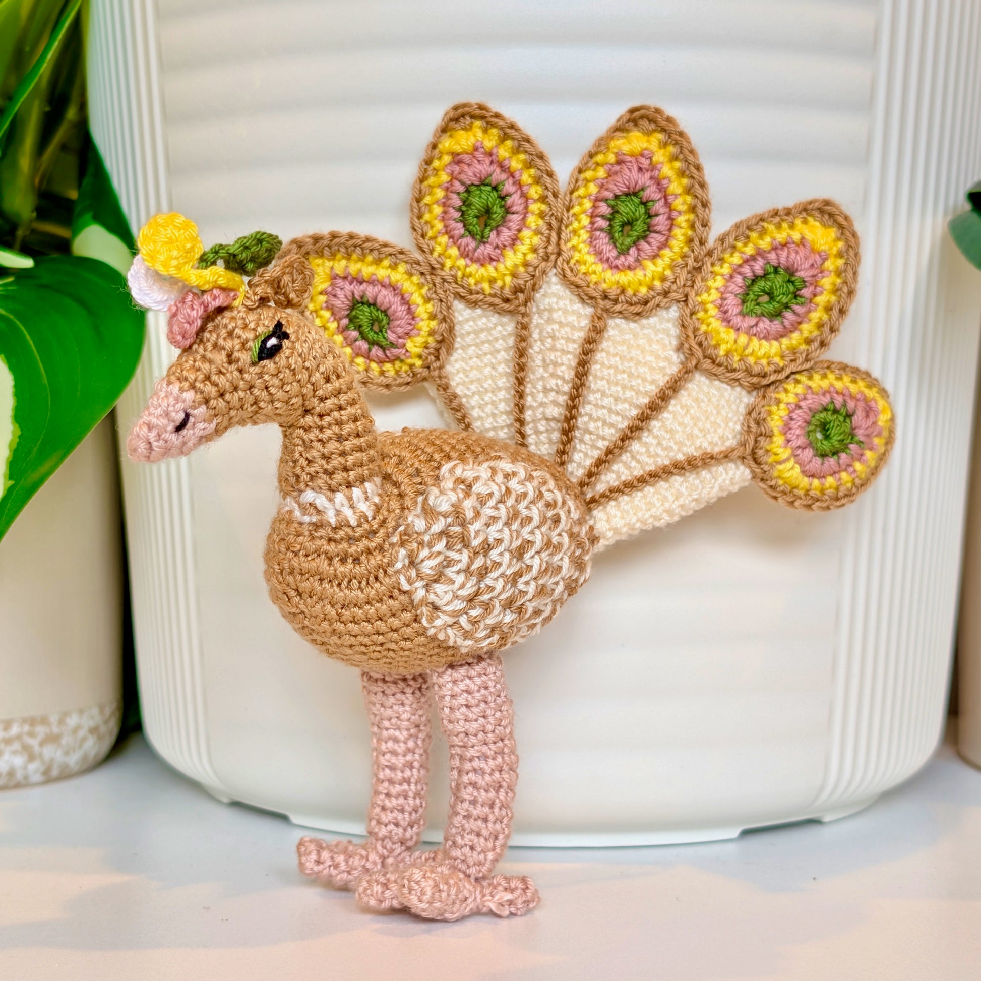 Sand brown crocheted peacock with ivory, yellow, moss green, and dusty pink accents