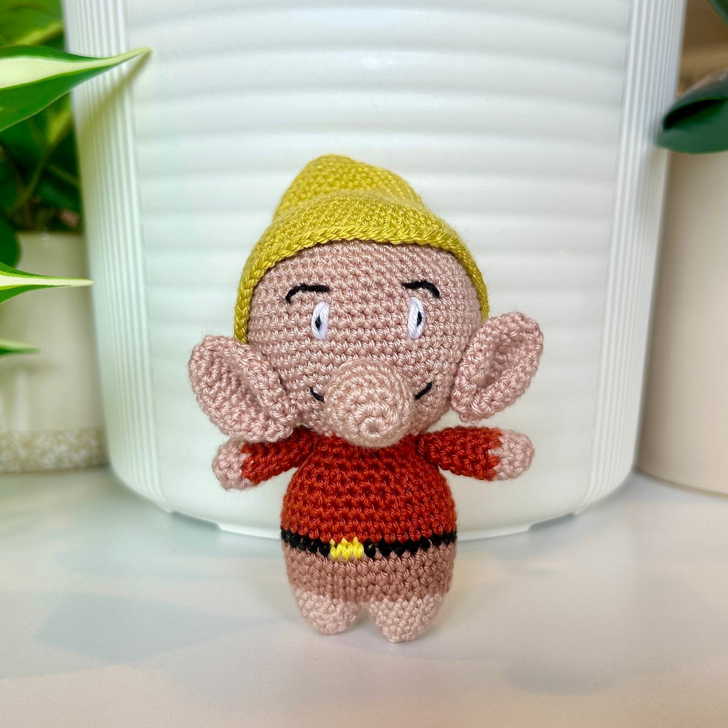 Happy crocheted troll wearing a pointy chartreuse hat, terracotta shirt, and mocha-colored shorts