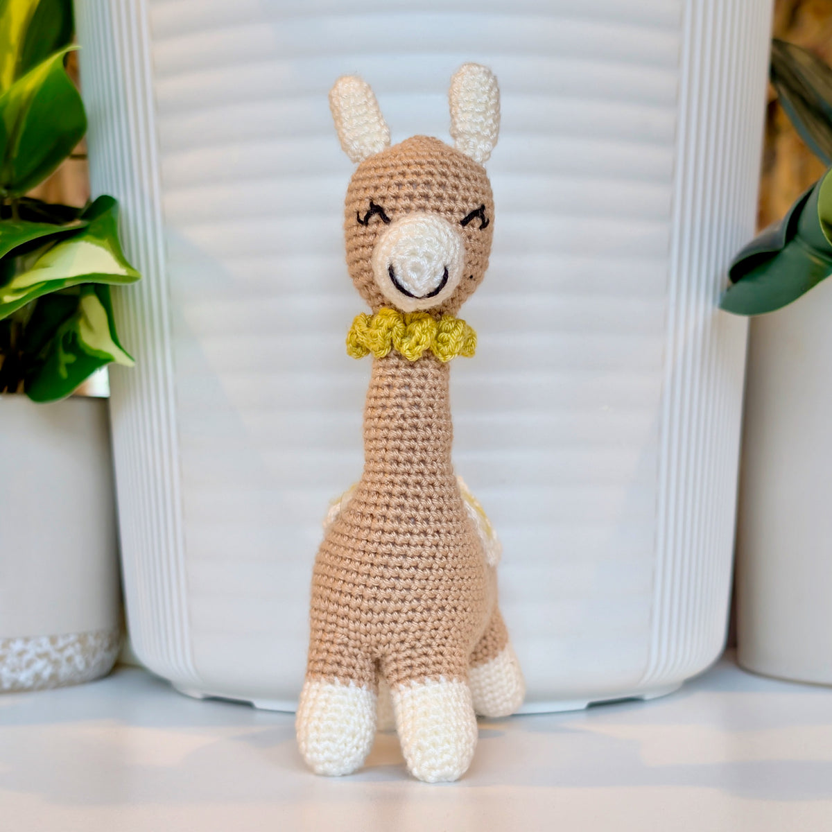 Front of crocheted vicuna llama beige plush with a white and chartreuse saddle and a chartreuse necklace
