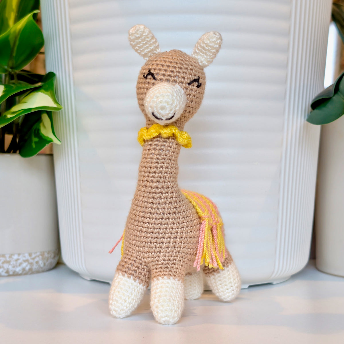 Crocheted vicuna llama beige plush with a yellow and pink saddle and a yellow necklace