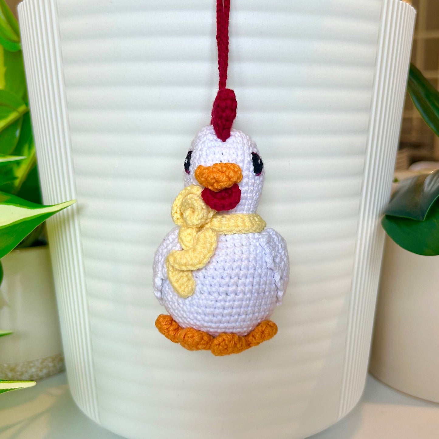 white crocheted chicken charm with a ruby red comb and a curly dark cream scarf around its neck