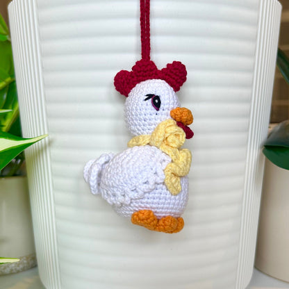 Left side profile of white crocheted chicken charm with a ruby red comb and a curly dark cream scarf around its neck