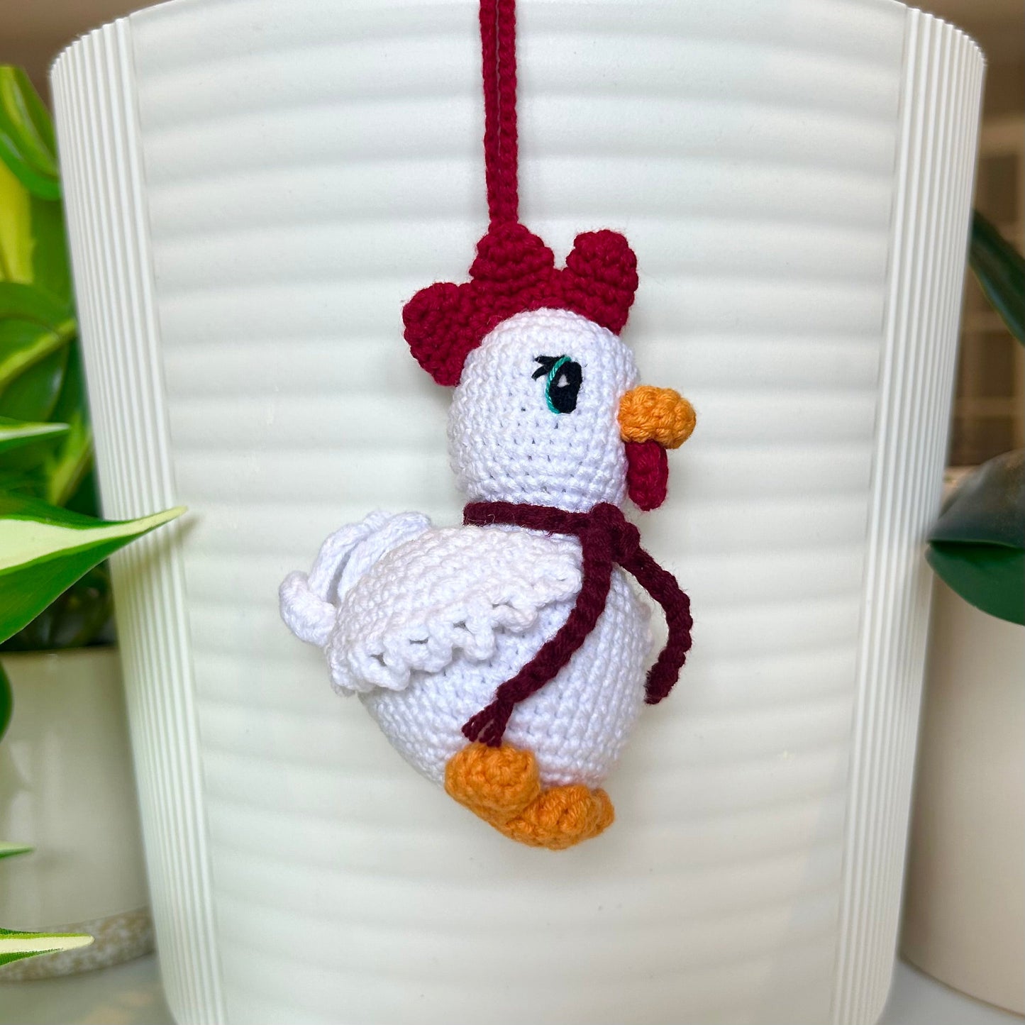 left side profile of white crocheted chicken charm with a ruby red comb and a dark maroon scarf