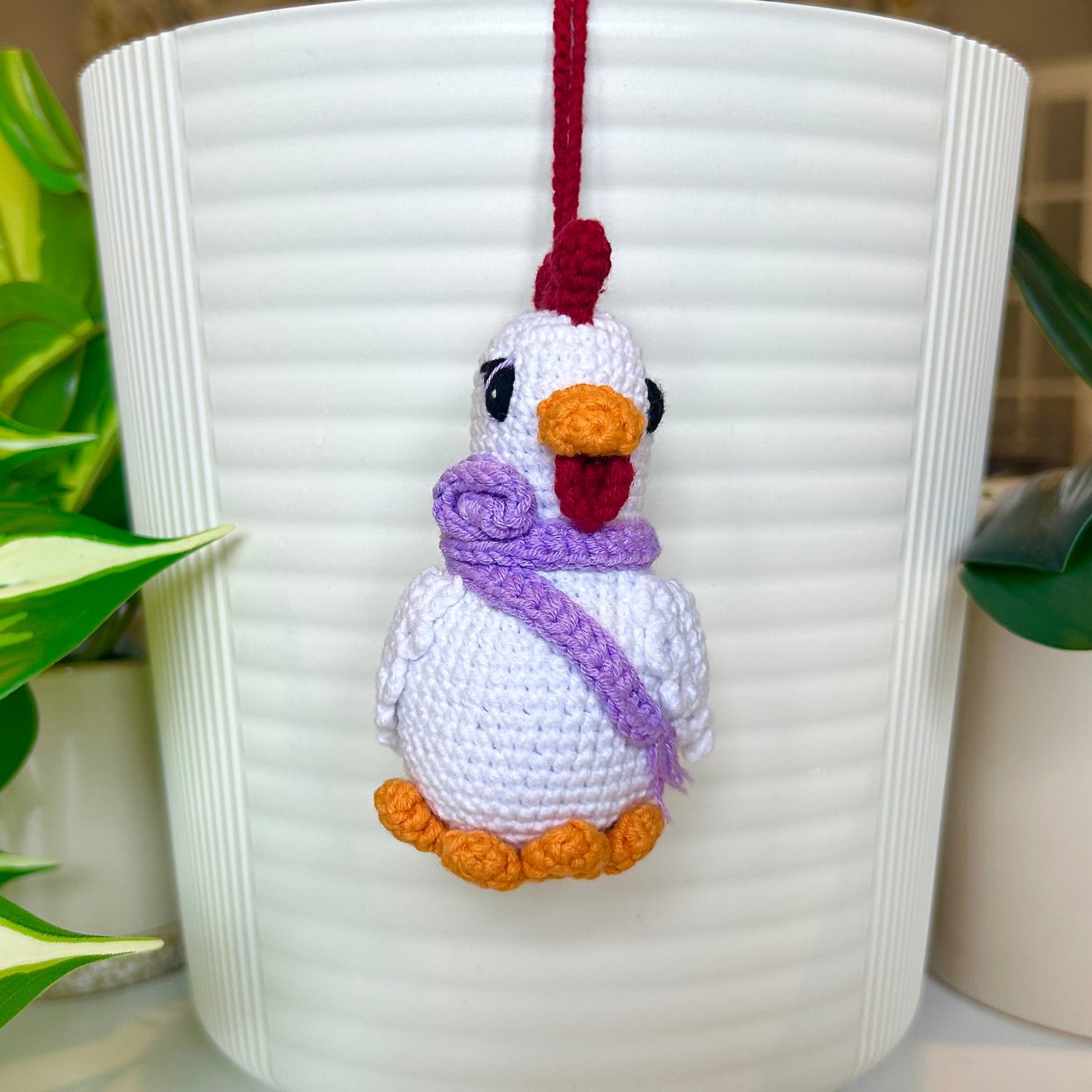 white crocheted chicken charm with a ruby red comb and a curly lavender scarf