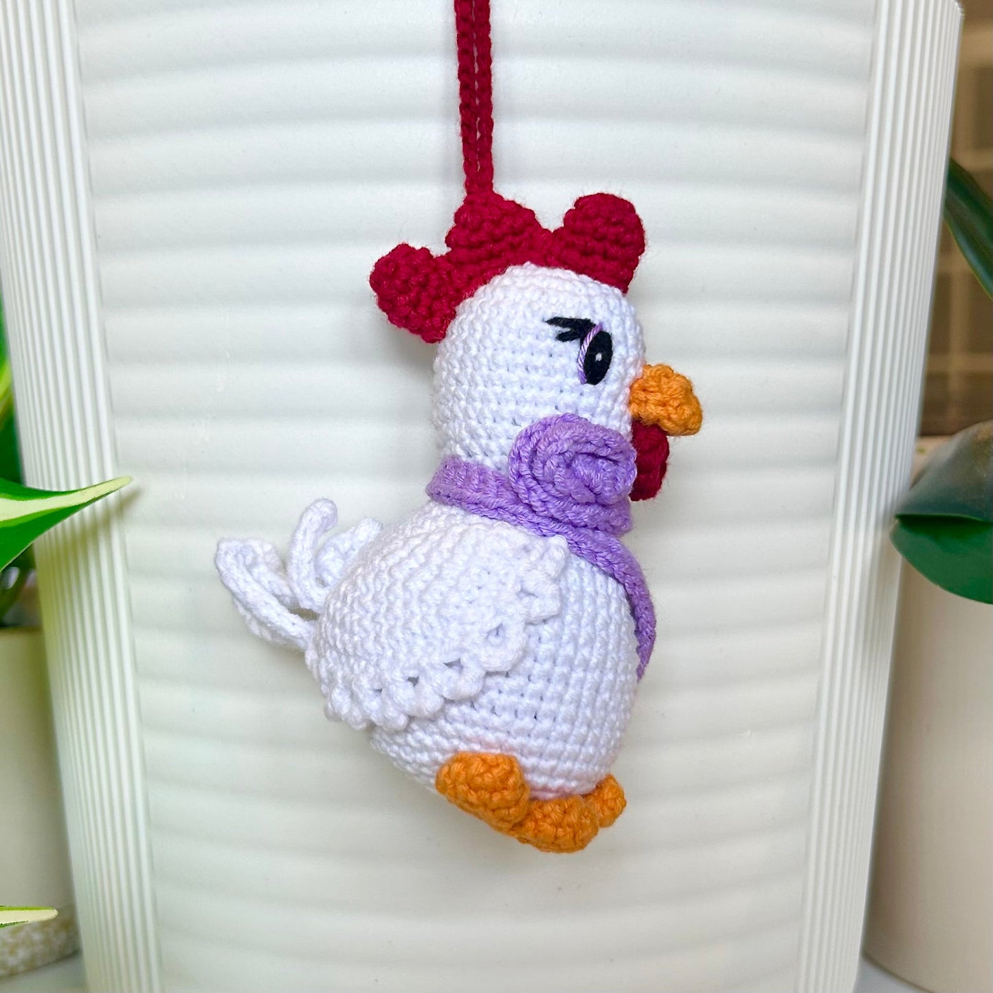left side profile of white crocheted chicken charm with a ruby red comb and a curly lavender scarf