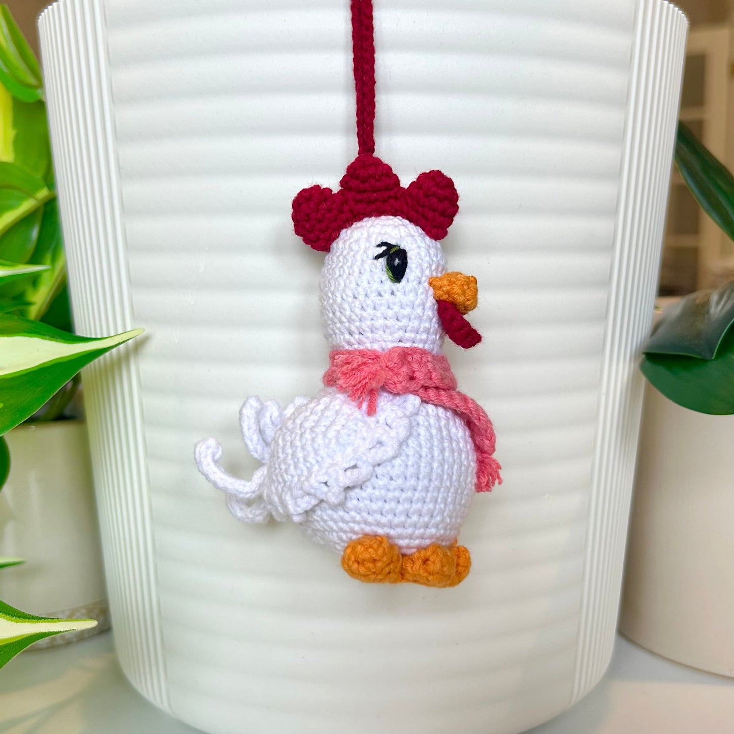 Left side profile of white crocheted chicken charm with a ruby red comb and a light carmine pink scarf