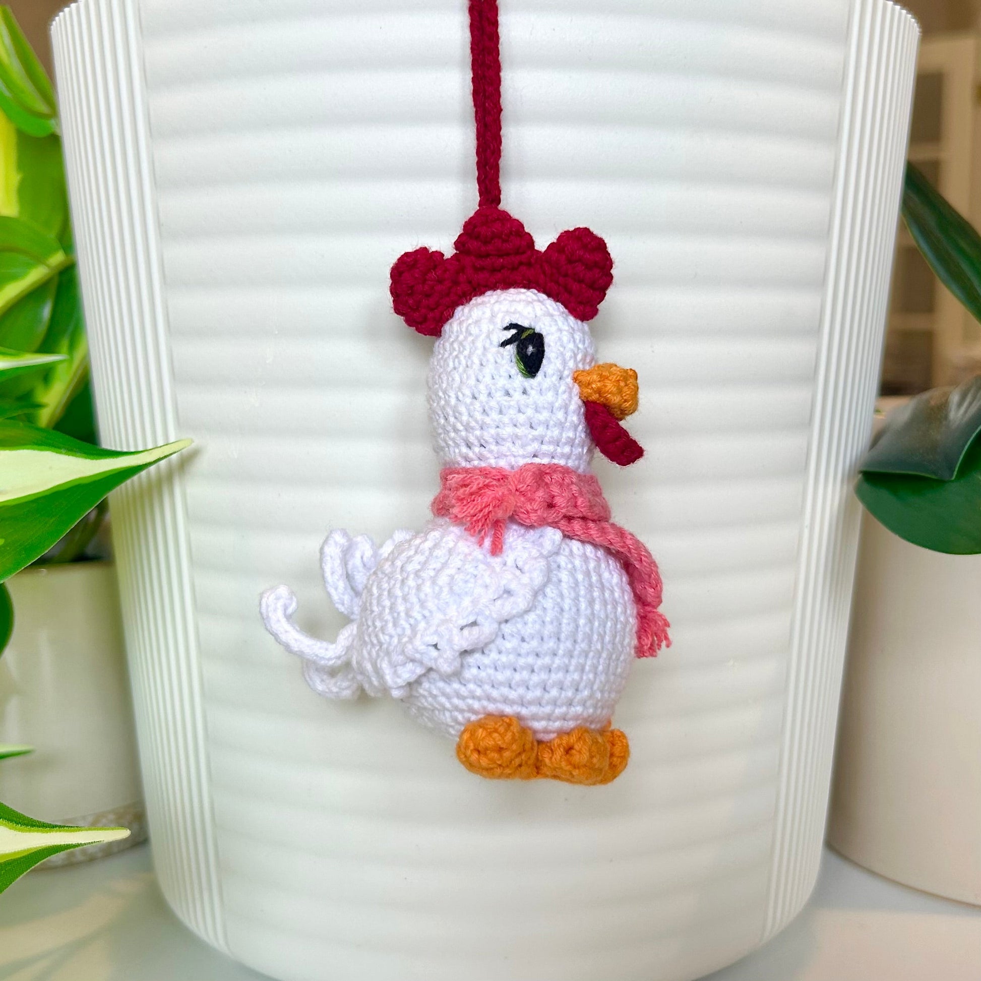 Left side profile of white crocheted chicken charm with a ruby red comb and a light carmine pink scarf