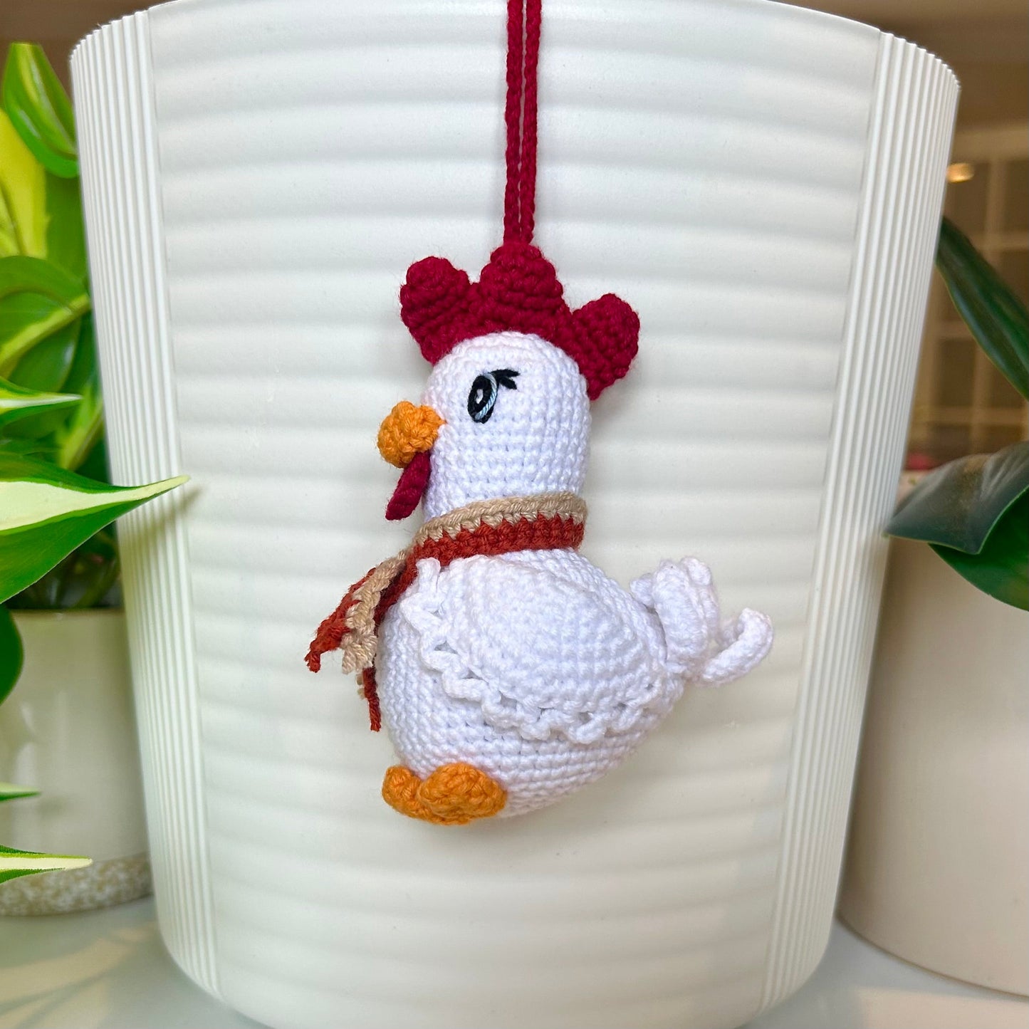 right side profile of a white crocheted chicken charm with a ruby red comb and a terracotta and tan scarf