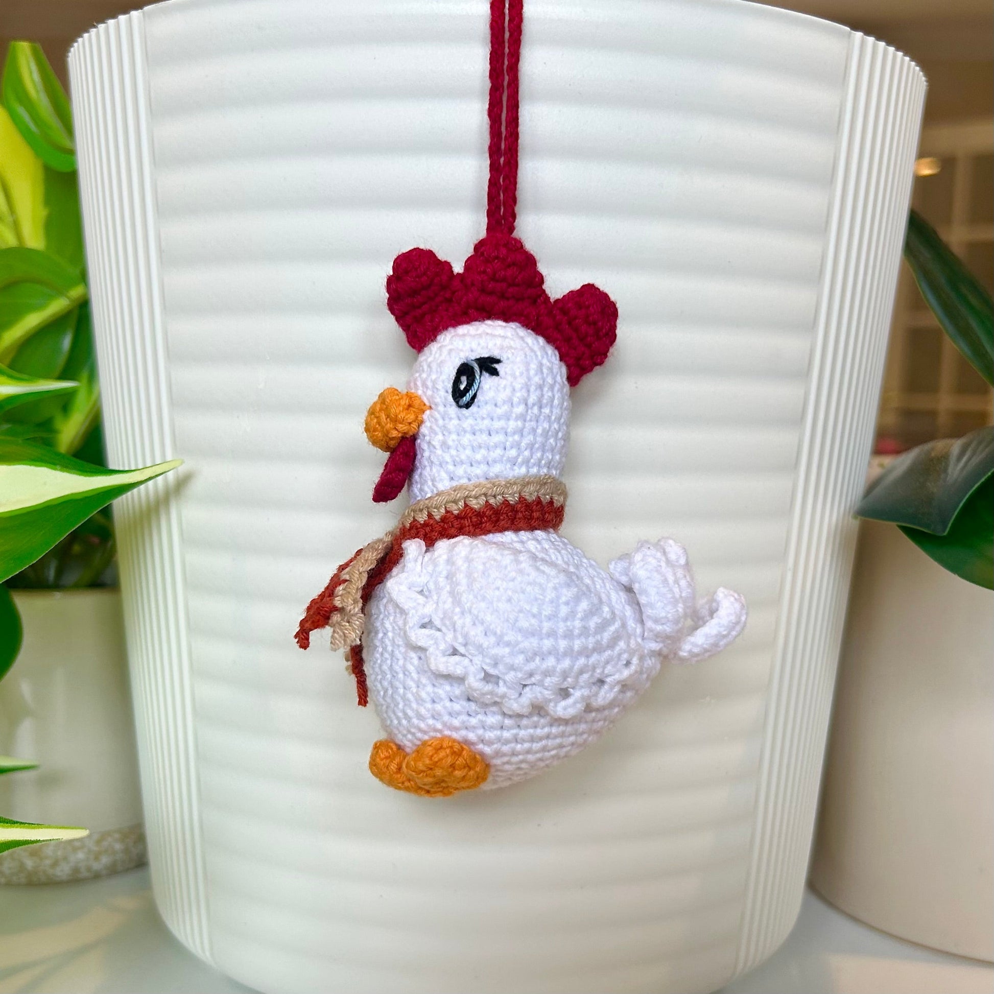 right side profile of a white crocheted chicken charm with a ruby red comb and a terracotta and tan scarf