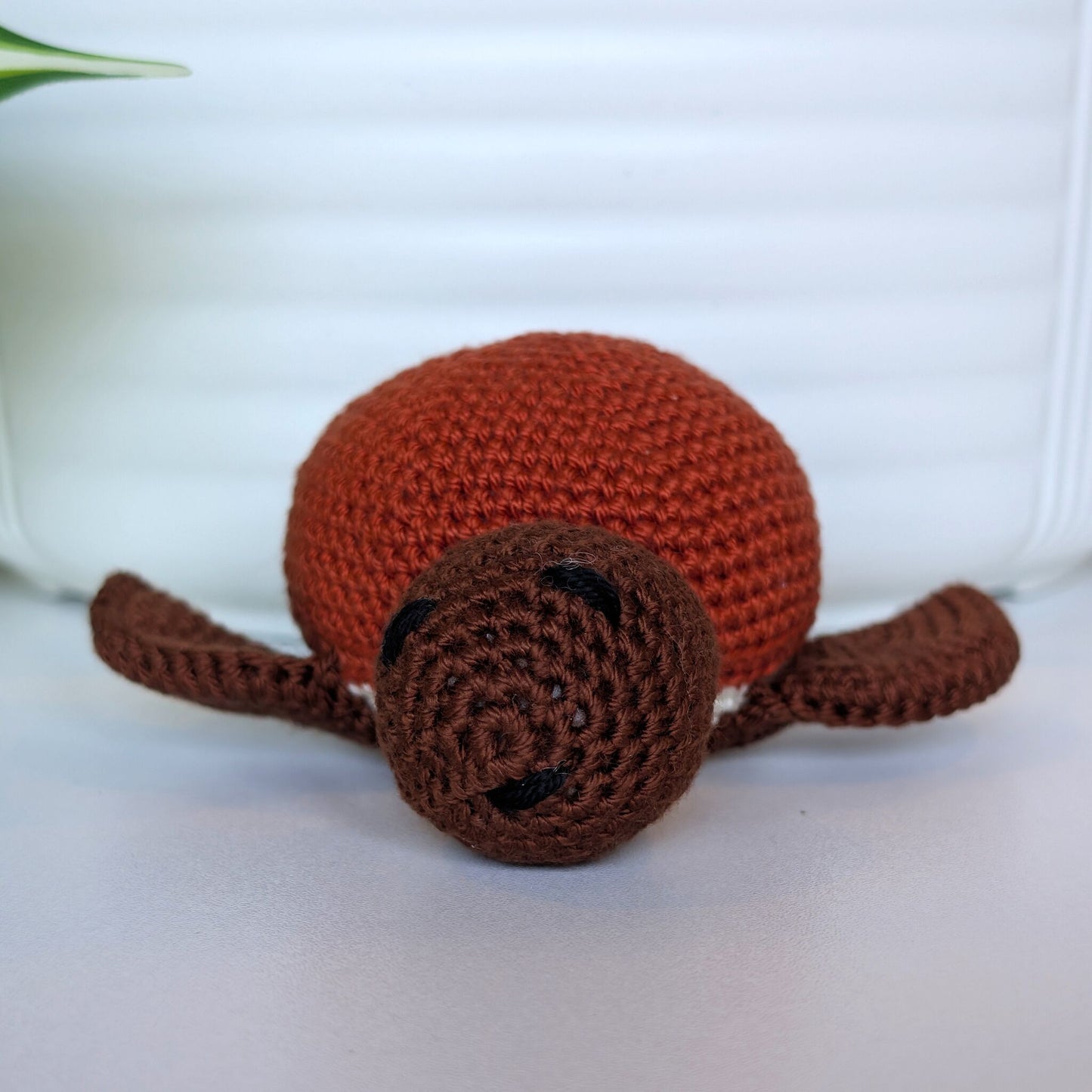 Front view of crocheted sea turtle plush with brown body and terracotta colored shell