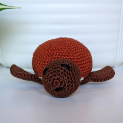 Front view of crocheted sea turtle plush with brown body and terracotta colored shell