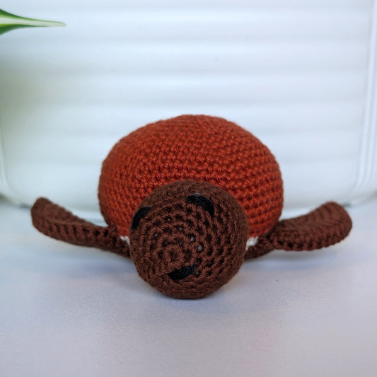 Front view of crocheted sea turtle plush with brown body and terracotta colored shell
