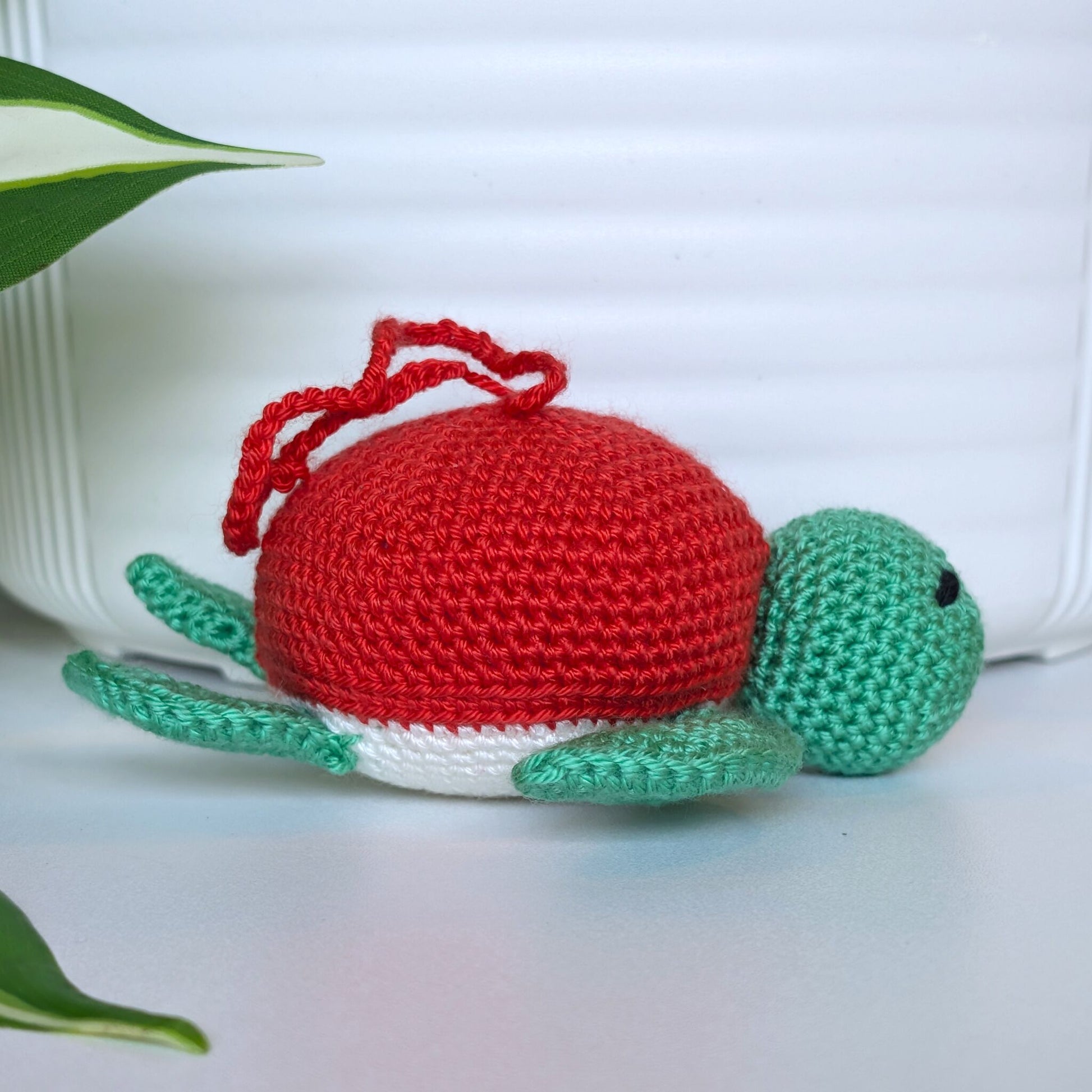Crocheted jade green body sea turtle with red orange shell and a string