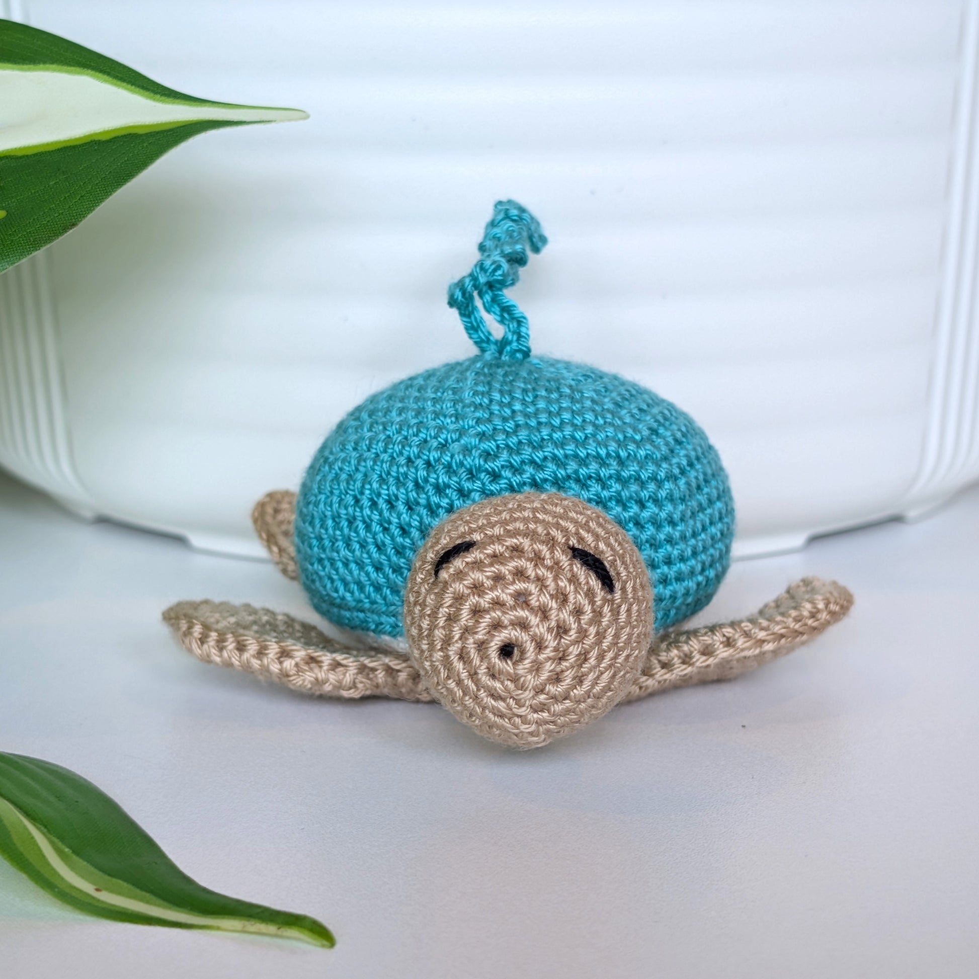 Front view of a crocheted Sea turtle with turquoise shell with beige body and a string
