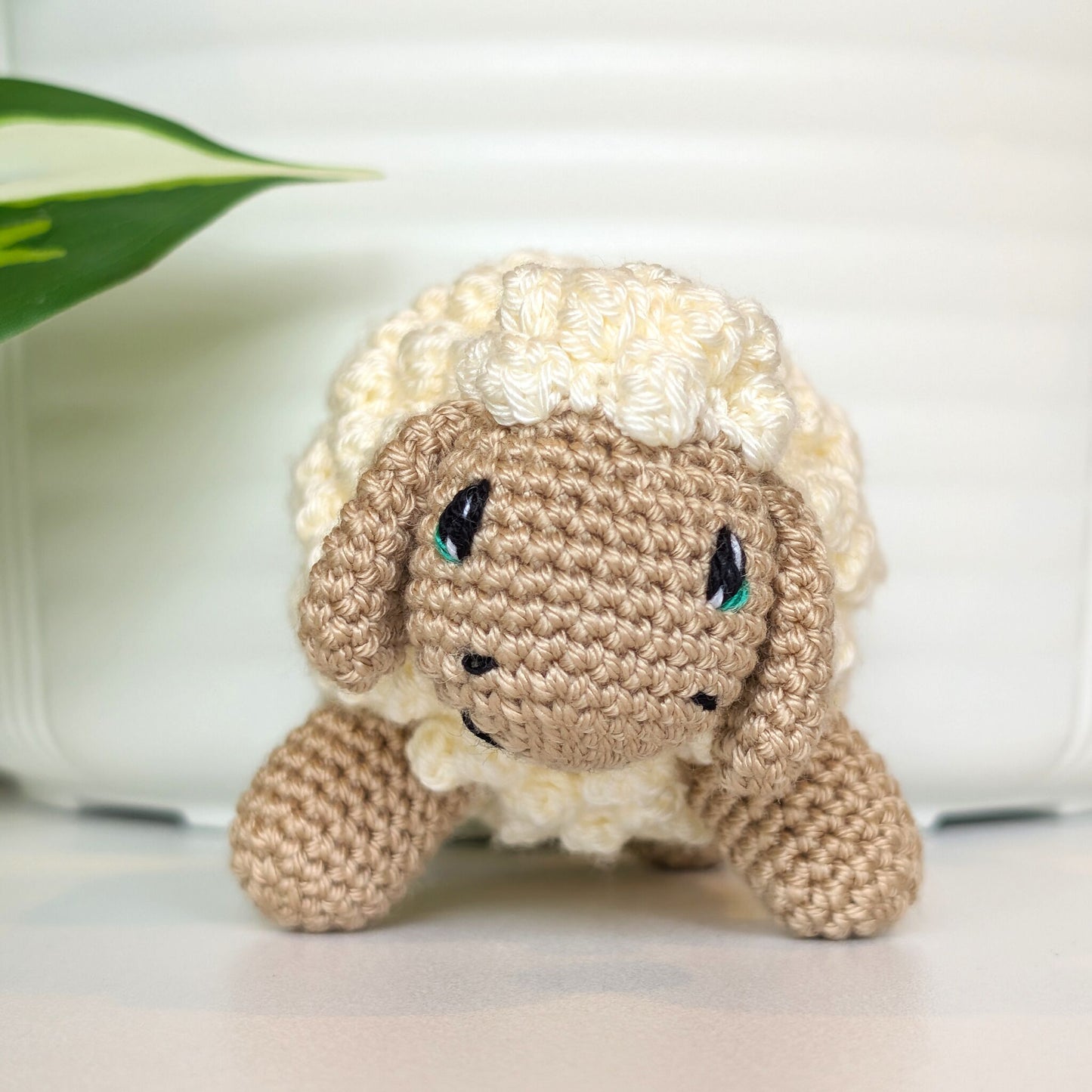 Front view of crocheted cream fleece sheep plush with beige body and emerald green eyes