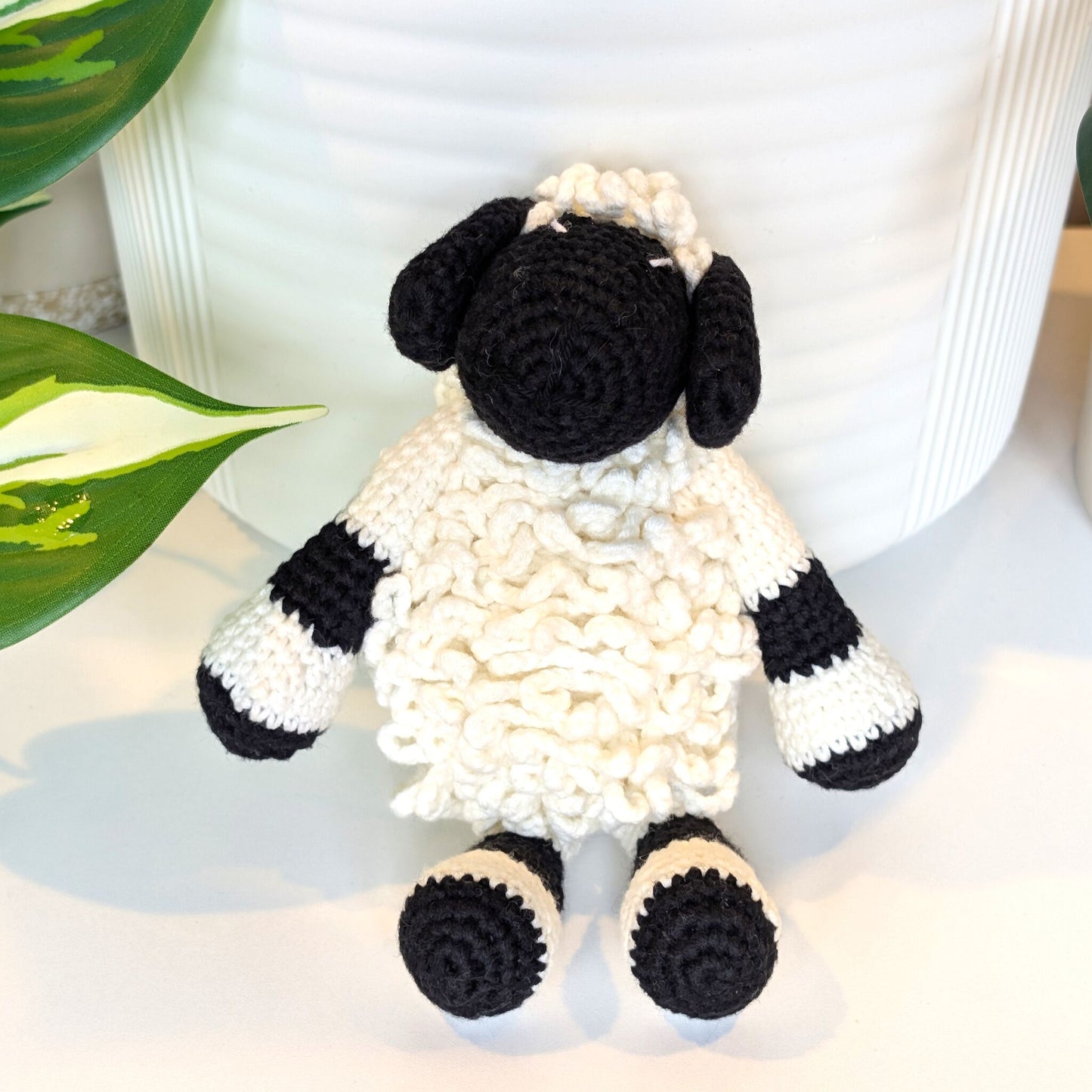 Front view of crocheted sheep toy with black and white pattern on a light background
