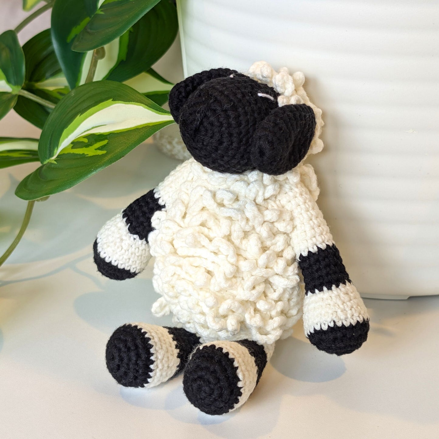 Side view of crocheted sheep toy with black and white pattern on a light background