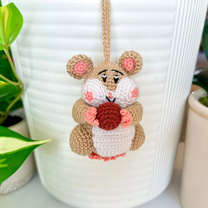 Crocheted beige hamster charm attached to a string, holding a terracotta ball