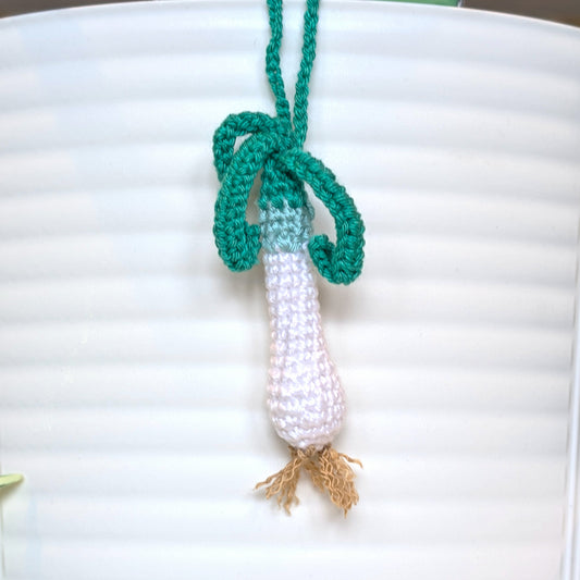Crocheted green and white spring onion bag charm attached to a string