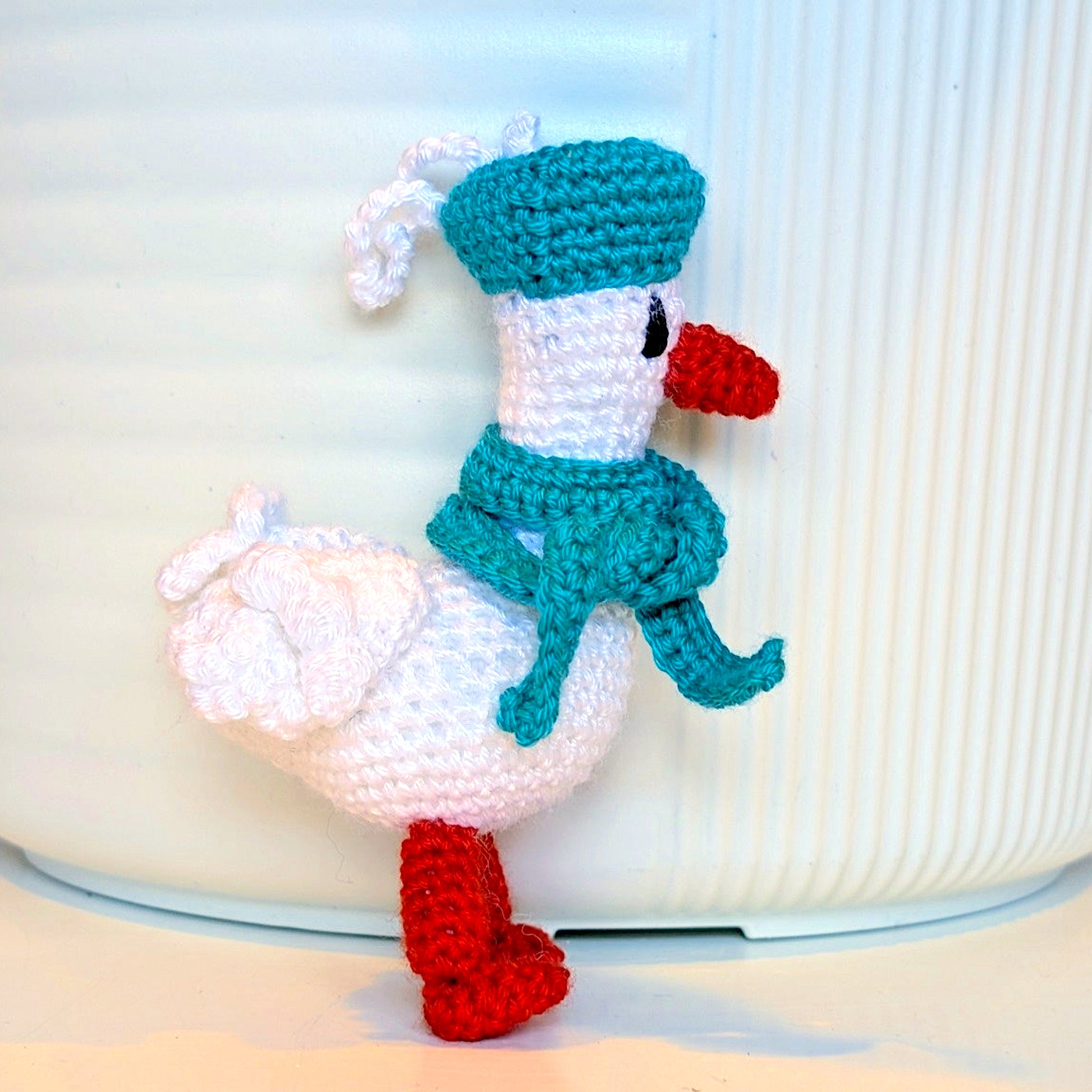 Crocheted duck keychain charm wearing a soft teal beret and scarf, attached to a string