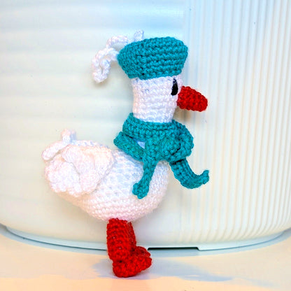 Crocheted duck keychain charm wearing a soft teal beret and scarf, attached to a string