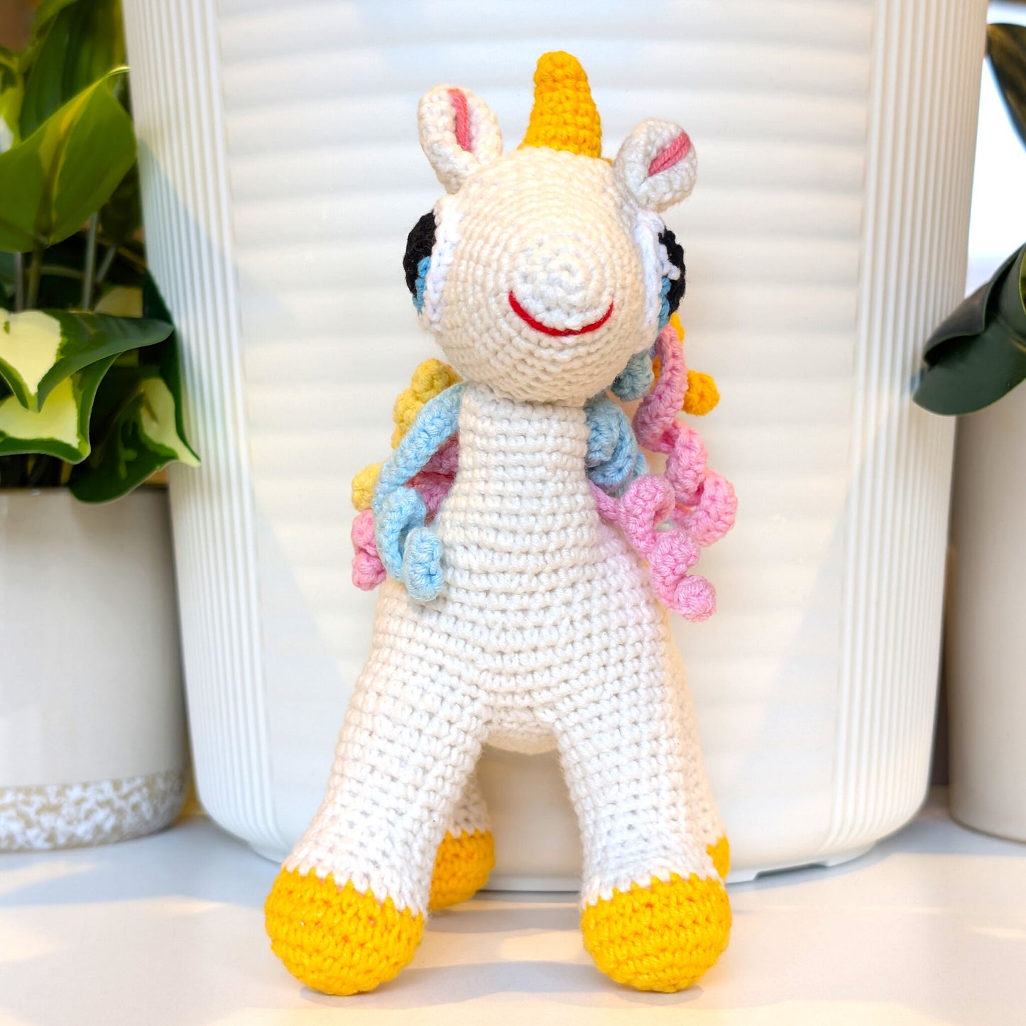 Front view of the crocheted unicorn toy with colorful mane and amber foot