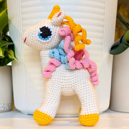 Side view of crocheted unicorn toy with colorful mane and amber feet