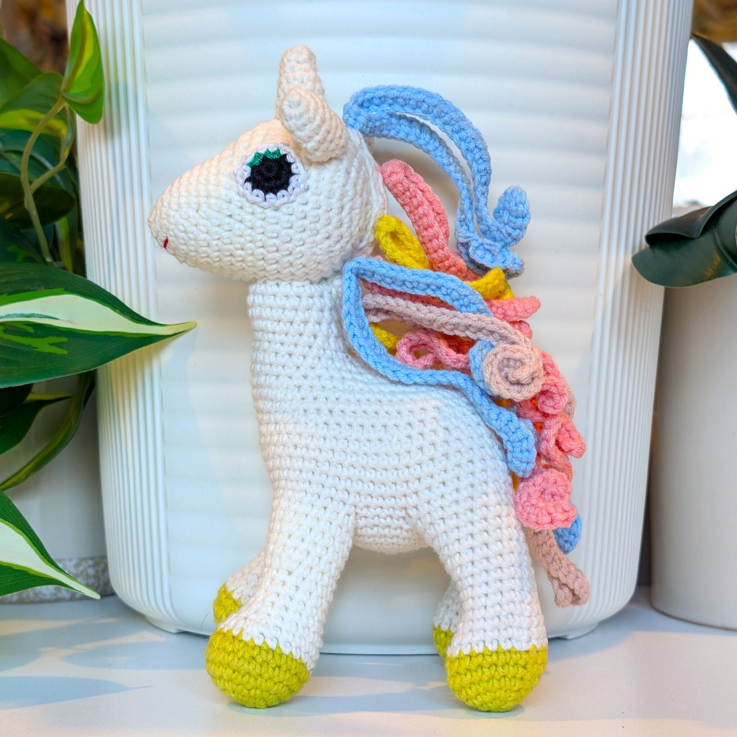 Crocheted unicorn plush with colorful blue, pink, dusty pink and yellow mane with chartreuse feet 