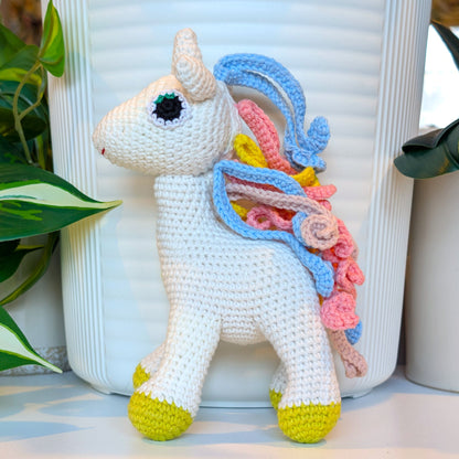 Crocheted unicorn plush with colorful blue, pink, dusty pink and yellow mane with chartreuse feet 