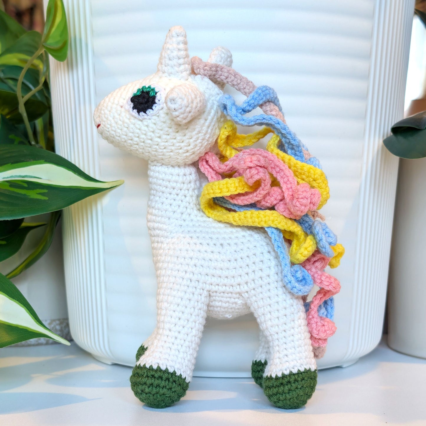 Crocheted plush unicorn toy in colorful mane and forest green feet