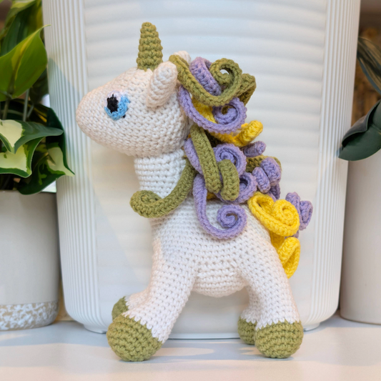 Crocheted unicorn plush toywith a lavender, yellow and light olive green mane with light olive feet