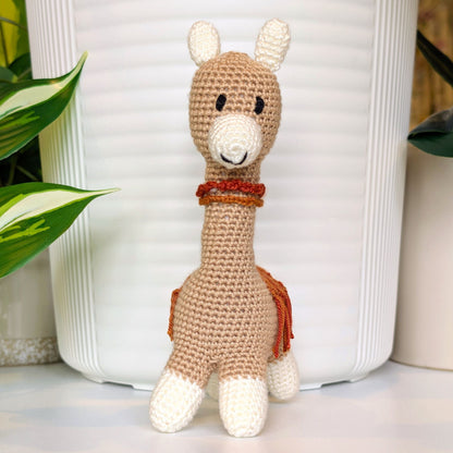 Front view of a crocheted Vicuna llama with a necklace and ginger, terracotta saddle