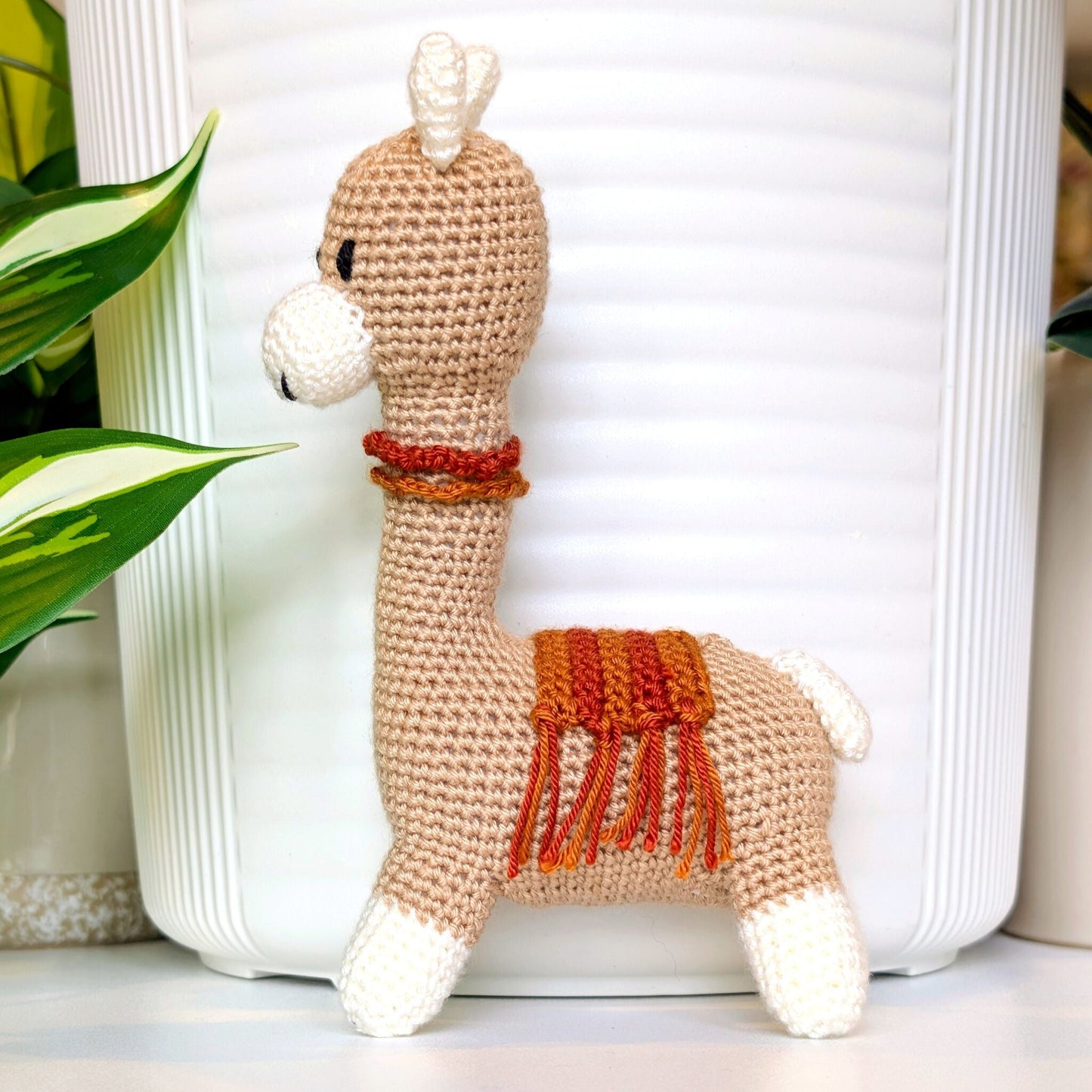 Crocheted Vicuna llama plush with a necklace and ginger, terracotta saddle