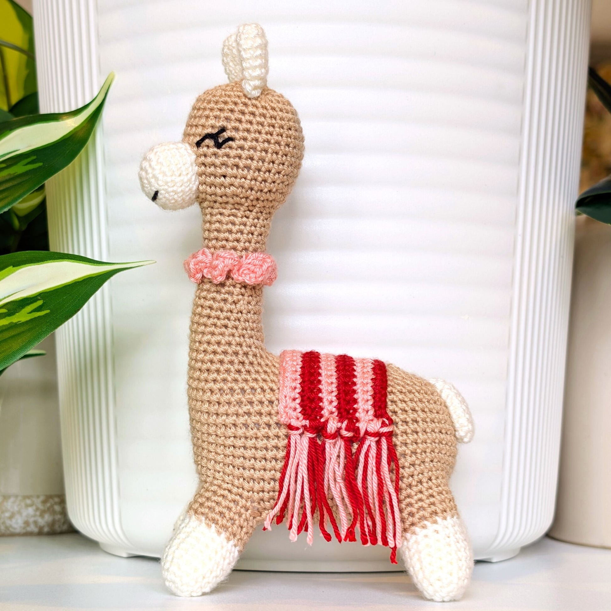 Crocheted Vicuna llama plush with a necklace and pink, red saddle
