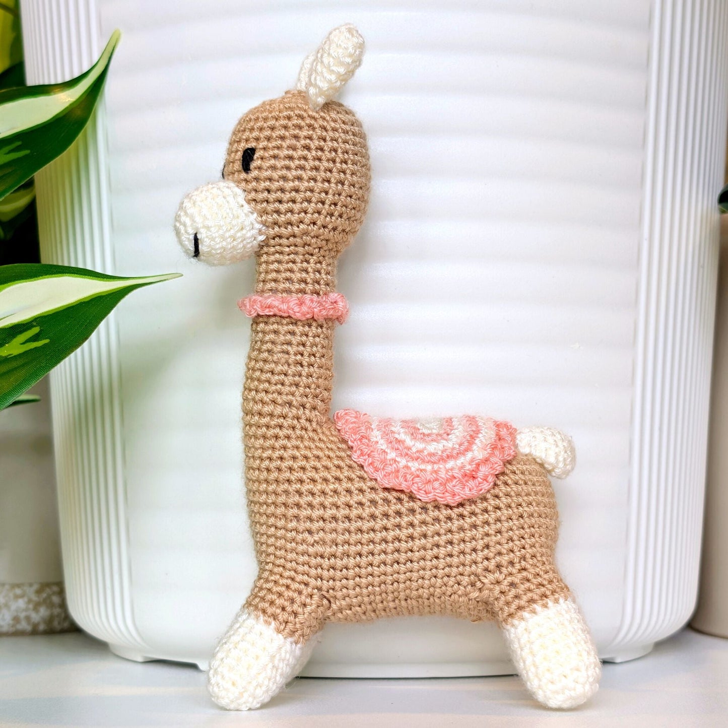 Crocheted Vicuna llama plush with a necklace and pink, white saddle