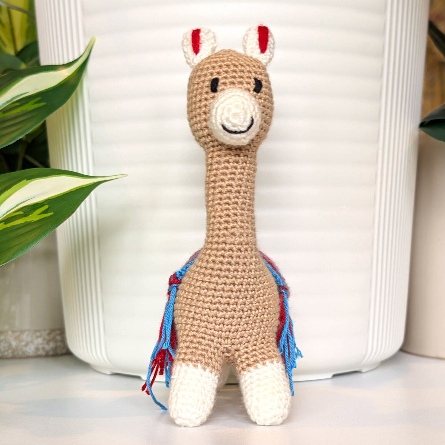 Front view of a crochet Vicuna llama with a red and azure saddle