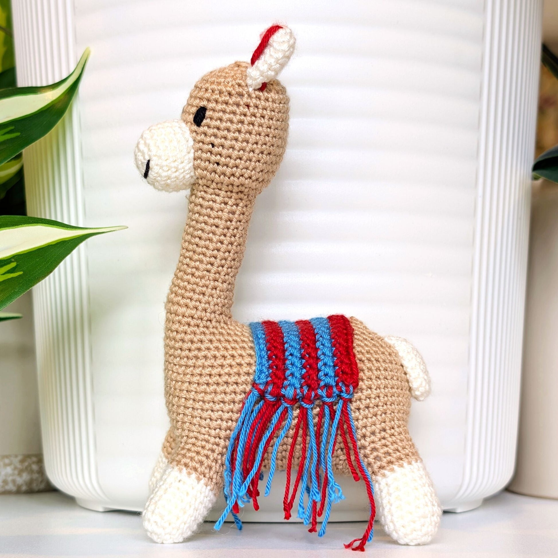 Side profile of crochet Vicuna llama with a red and azure saddle