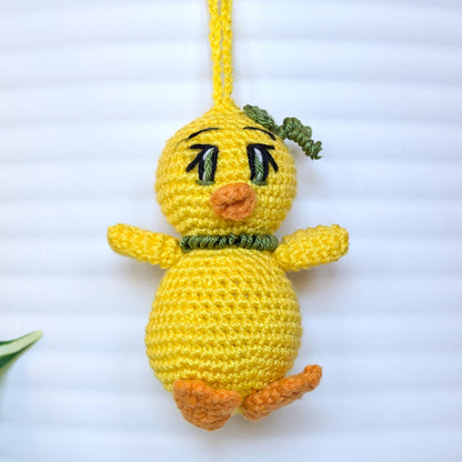 Crocheted yellow chick with green eyes and string wearing a hair accessory and necklace